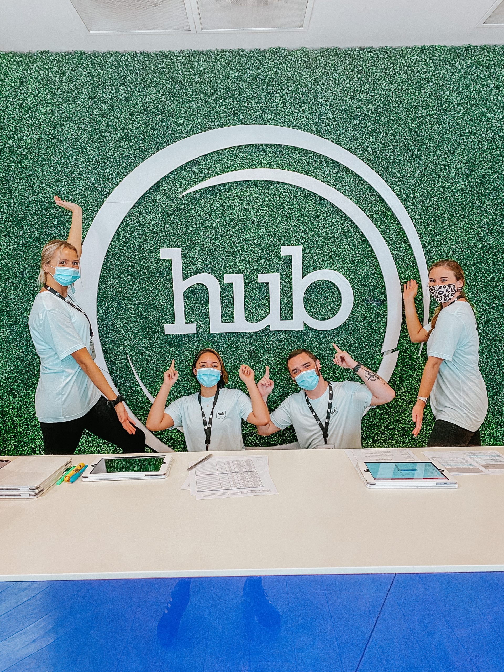 Four students posing for camera in front of Hub sign, wearing face masks
